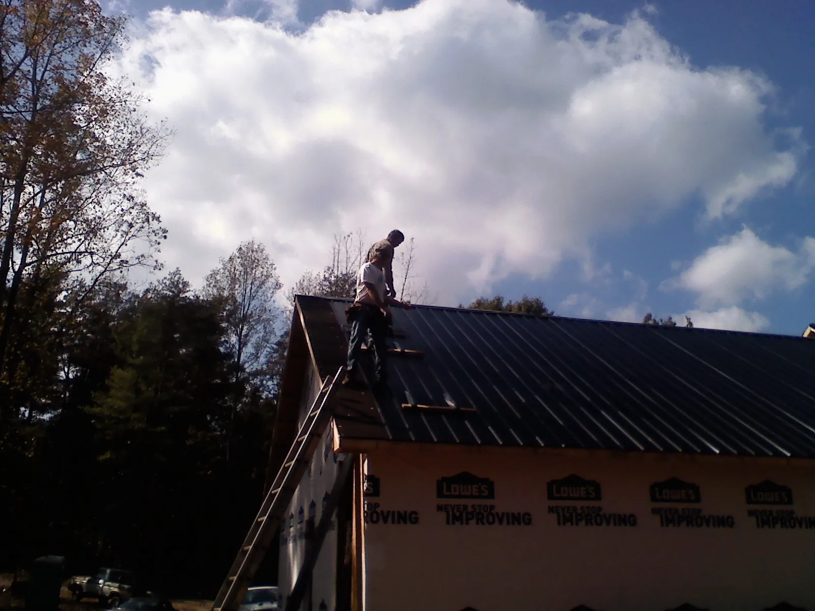 Roofer fastening dark metal panels high against a cloudy sky, from a Roof Inspection job in Monmouth